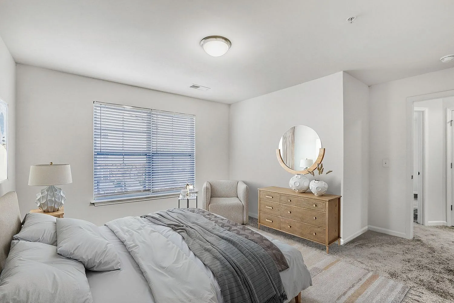 Primary bedroom, gray bedding, wood-style dresser, round mirror, carpet flooring