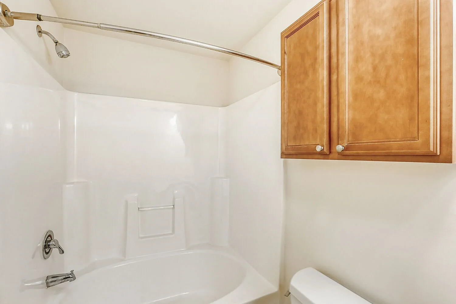 Bathroom, white subway tile surround, gold showerhead fixture, wood cabinetry, toilet