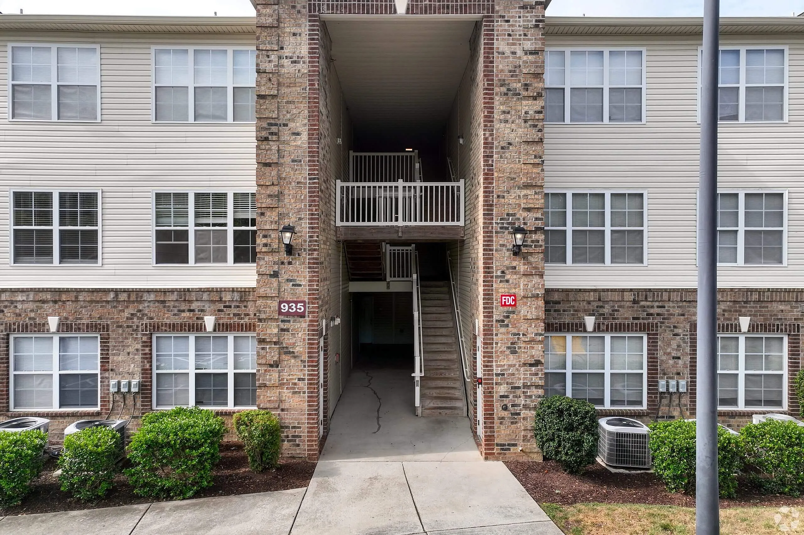Building entrance, brick facade, white framed windows, metal railings, landscaping