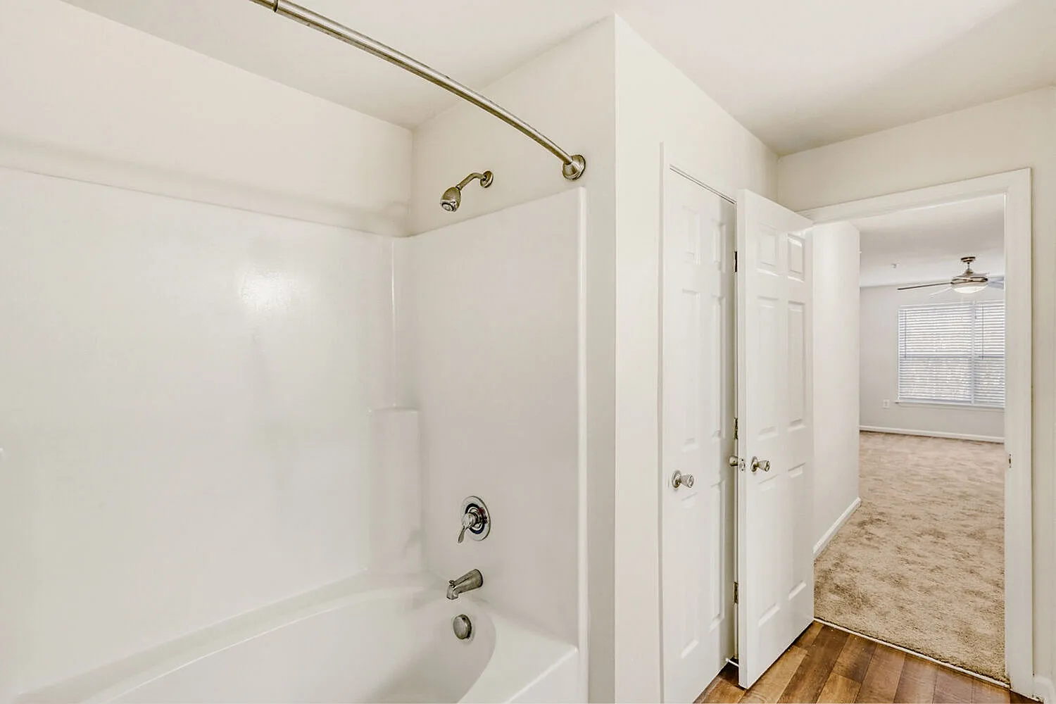 Primary bathroom, white subway tile surround, chrome fixtures, wood-style plank flooring
