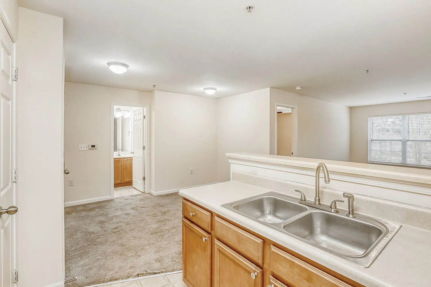 Kitchen with wood cabinetry, stainless steel sink, white countertops, wood-style plank flooring, open to dining space