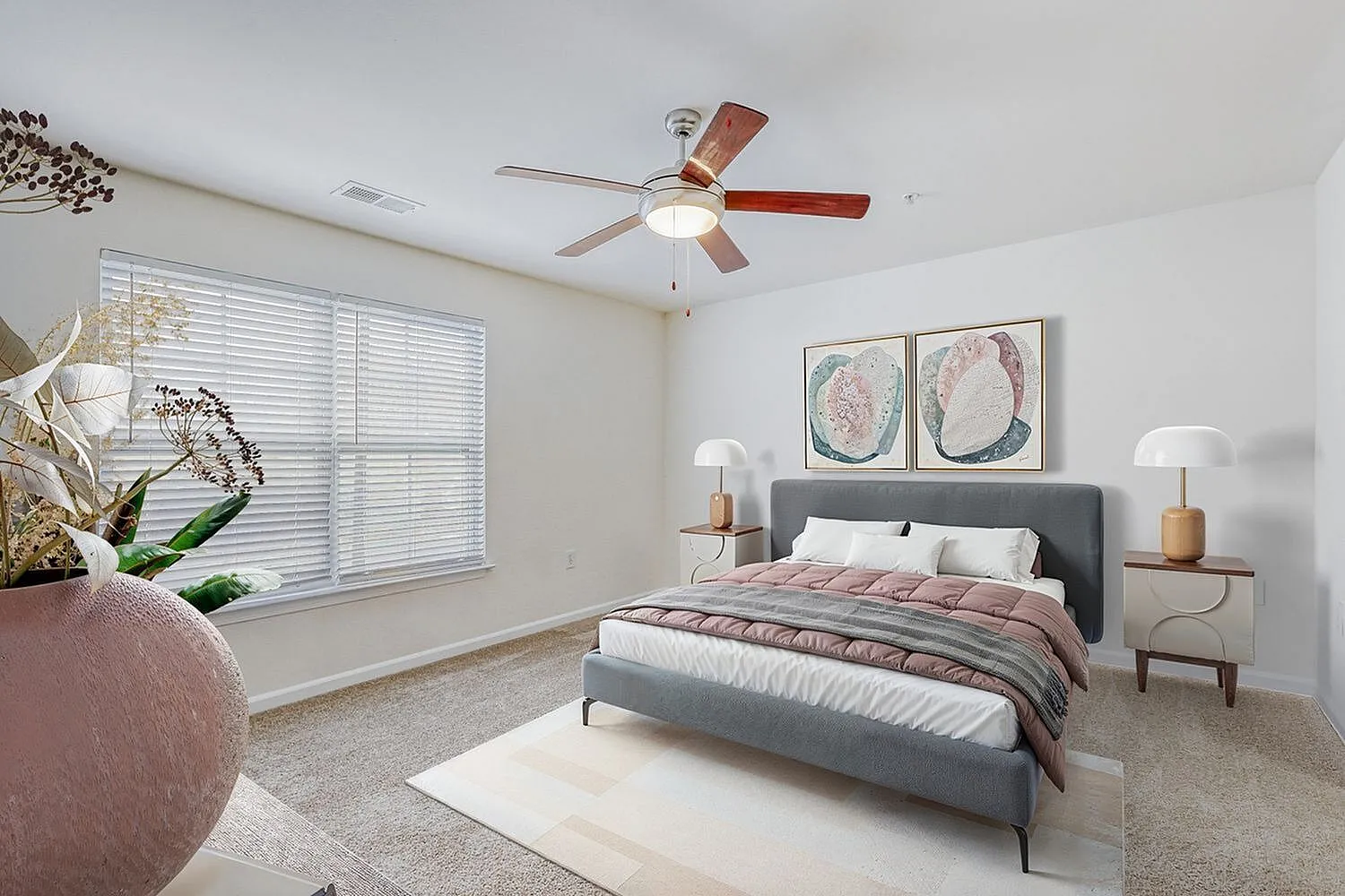 Primary bedroom, gray upholstered bed, wood nightstands, ceiling fan, framed botanical artwork