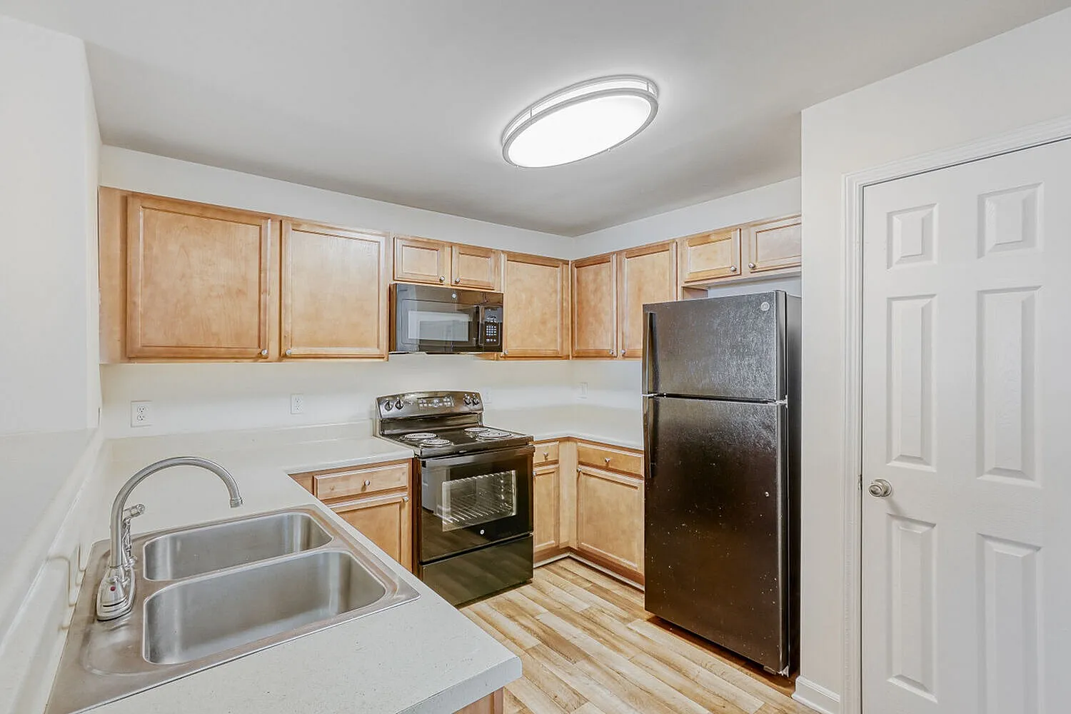Kitchen, light wood cabinetry, white countertops, stainless steel sink, black appliances, wood-style plank flooring