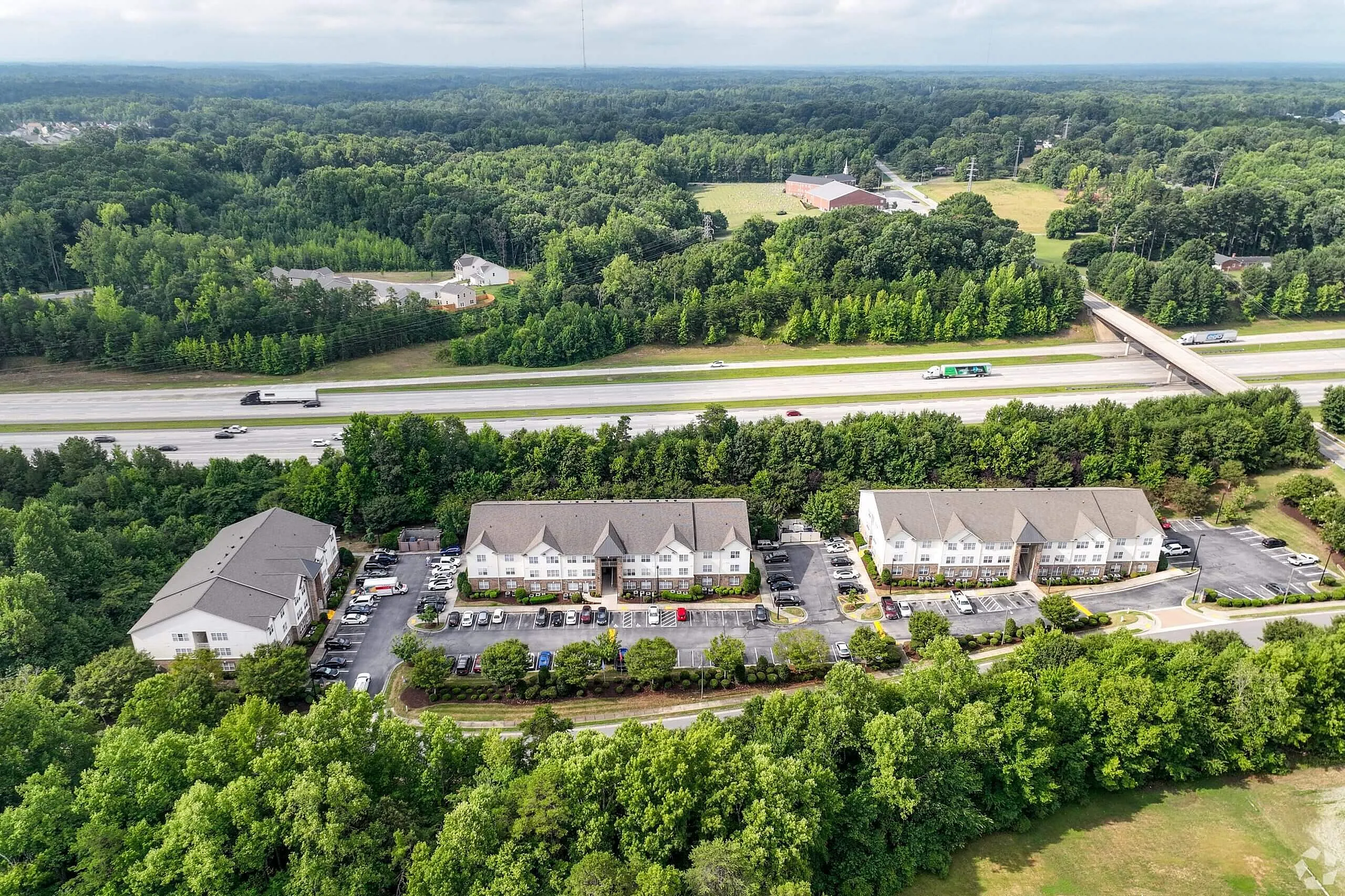 Aerial view of multi-building residential complex, parking areas, surrounding green landscape and waterway