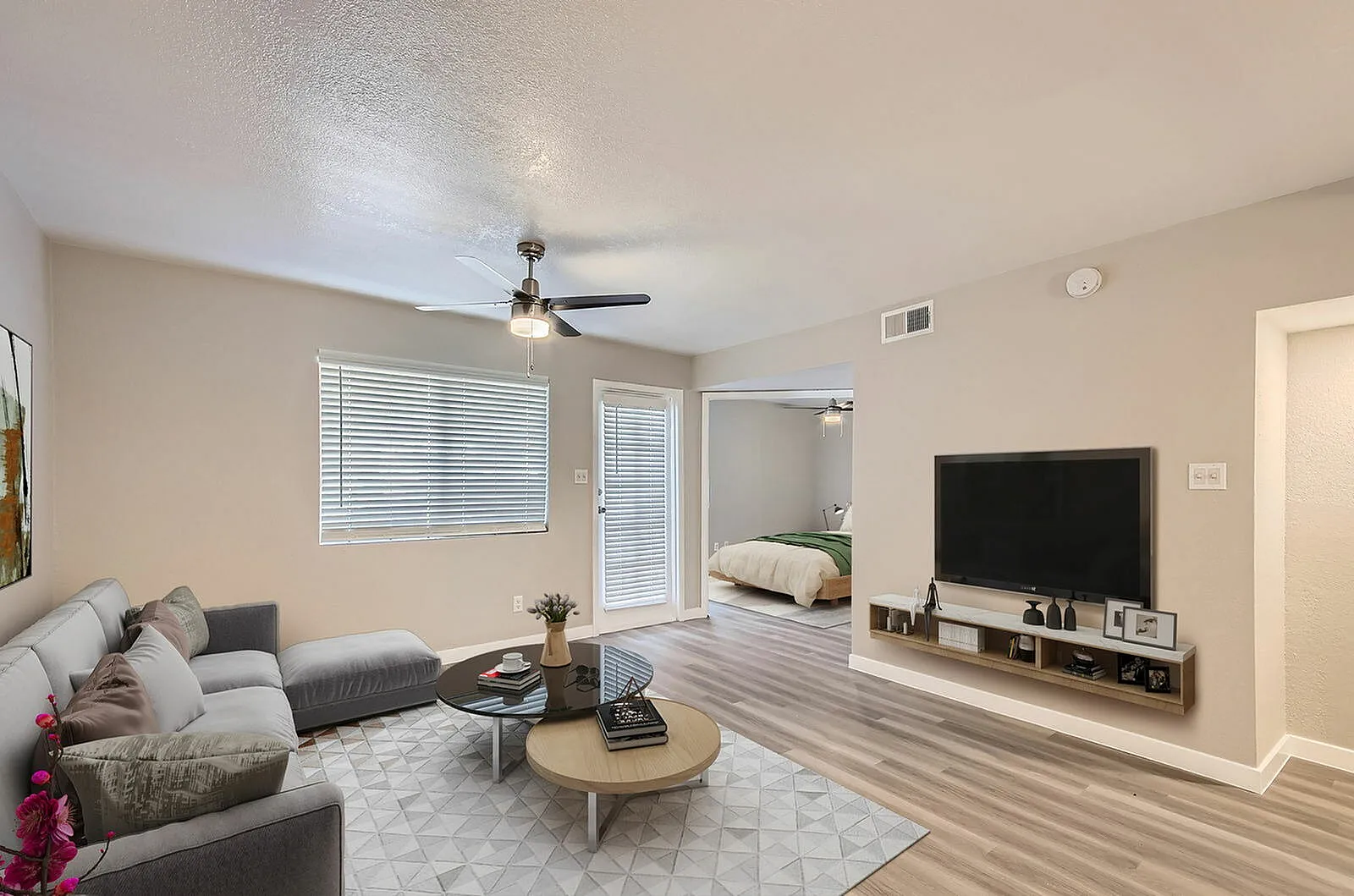 Living room, wood-style plank flooring, gray sectional sofa, flat-screen TV, ceiling fan