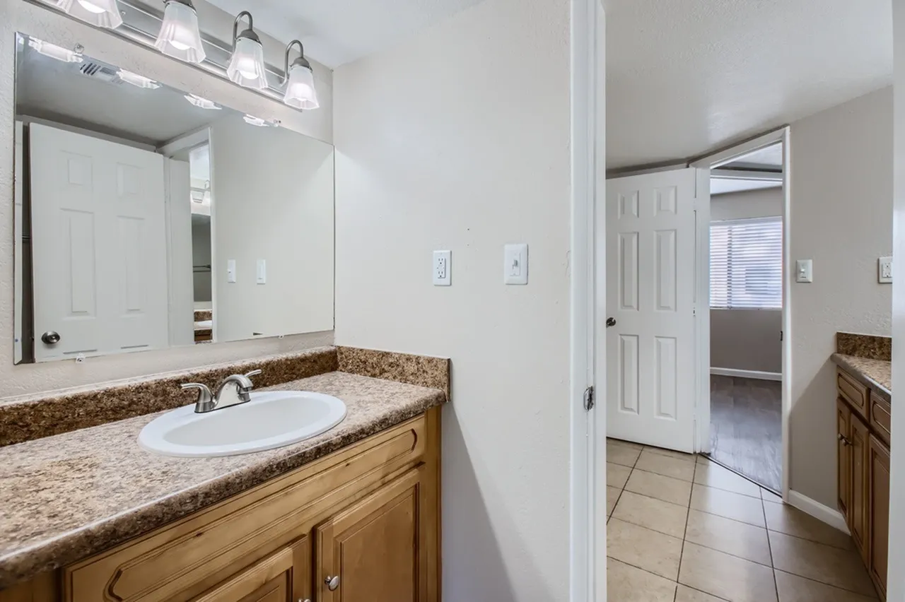 Primary bathroom, granite countertops, wood vanity cabinetry, large mirror with lighting