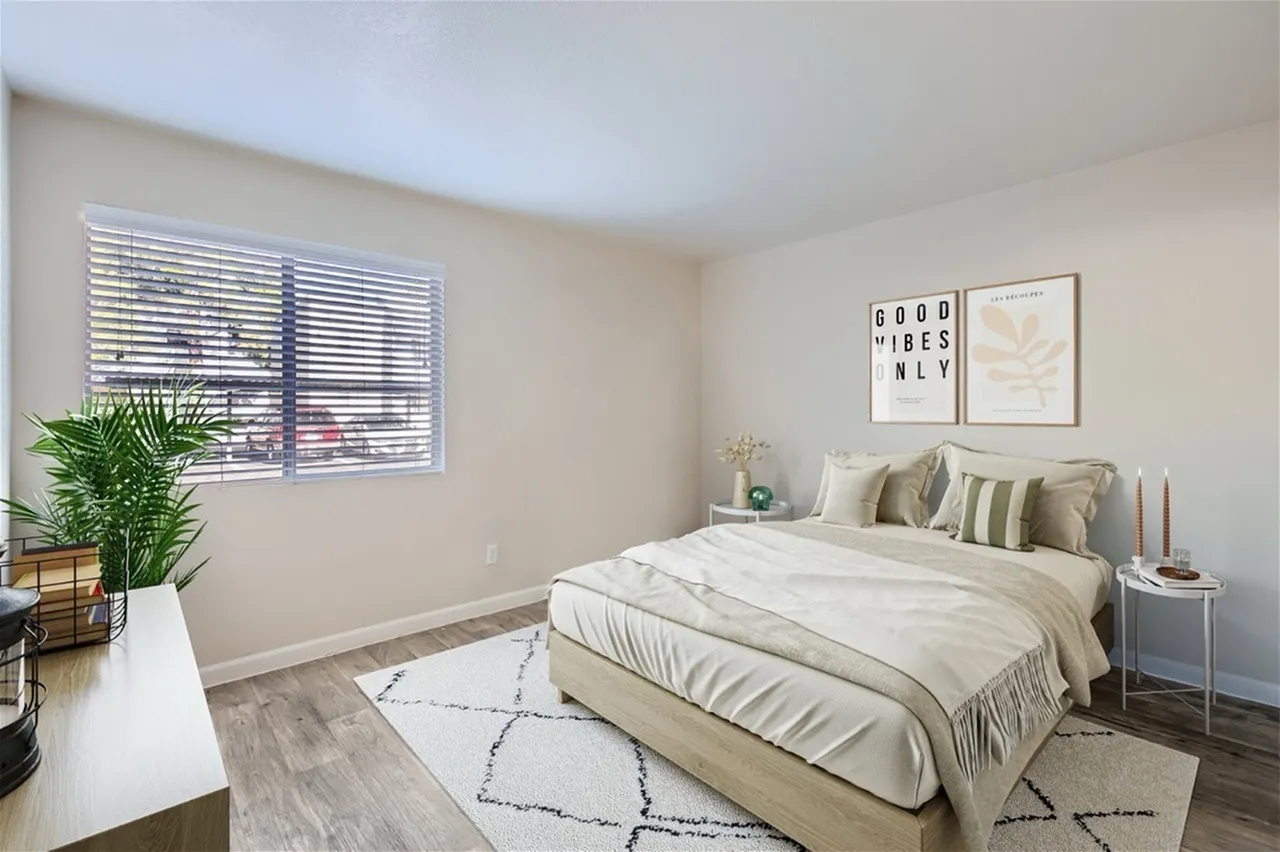 Primary bedroom, wood-style plank flooring, neutral bedding, framed wall art, plant accent