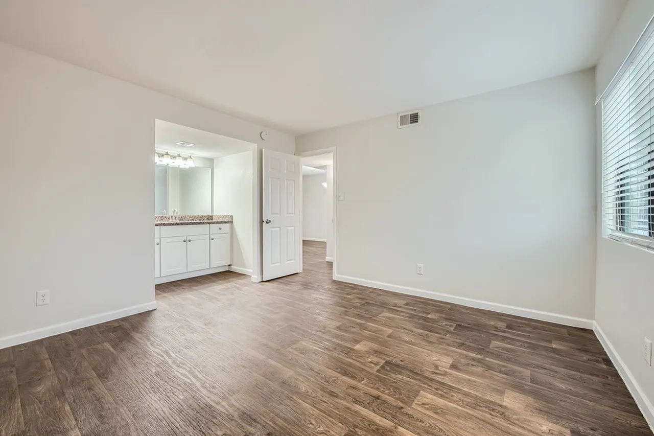 Primary bedroom, wood-style plank flooring, white vanity cabinetry, ensuite bathroom access