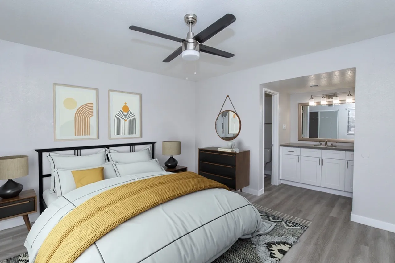 Primary bedroom, yellow bedding, wood-style plank flooring, ceiling fan, ensuite bathroom