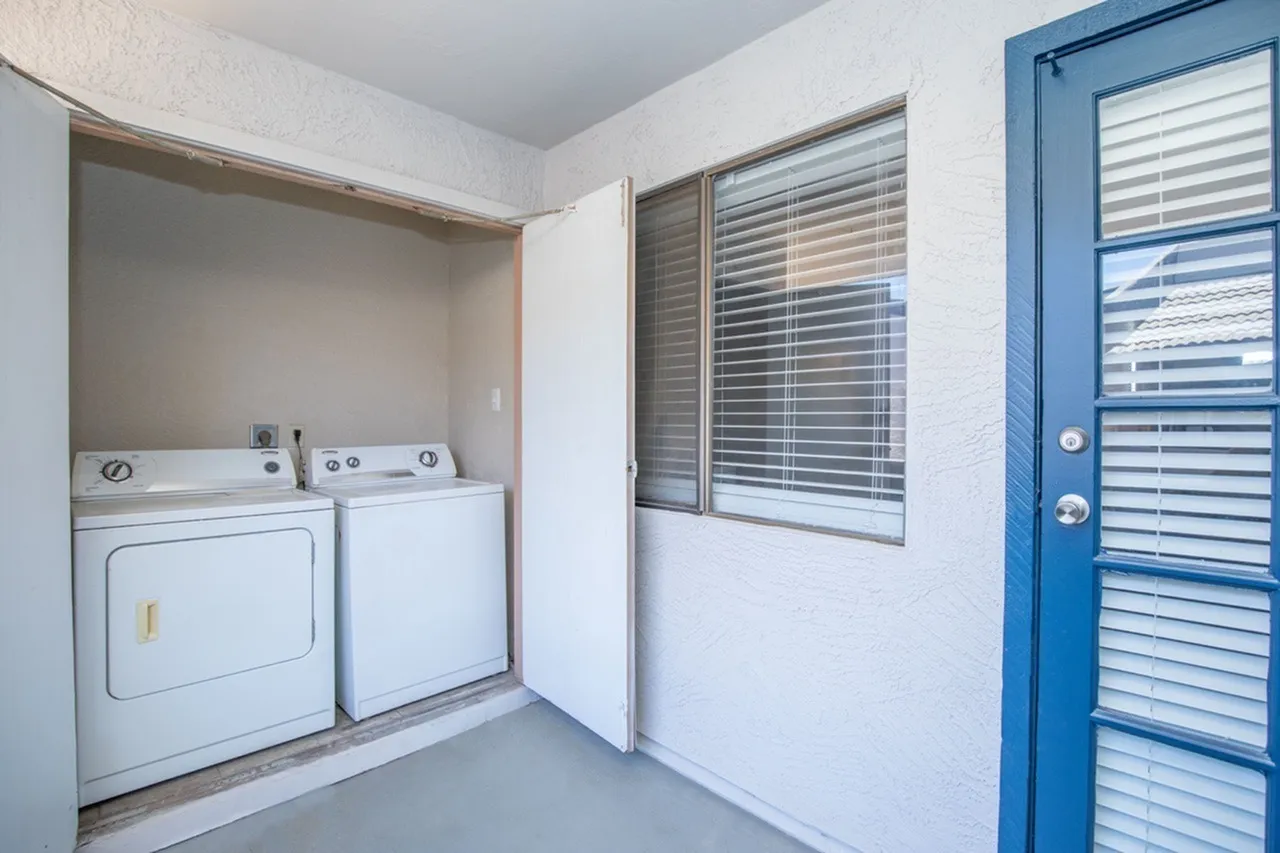 Laundry room, stacked washer and dryer, white appliances, louvered window, blue entry door