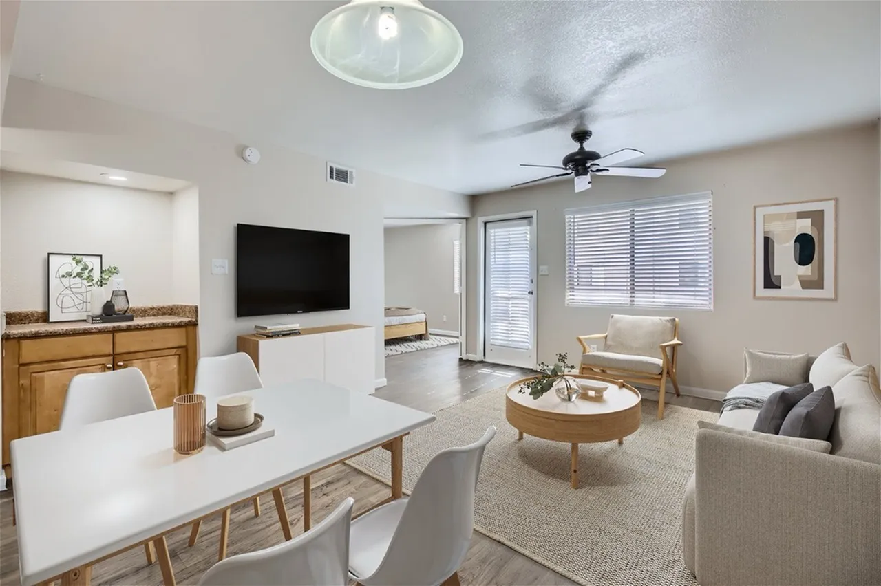 Open concept living and dining area, wood-style plank flooring, ceiling fan, white dining table with wood base