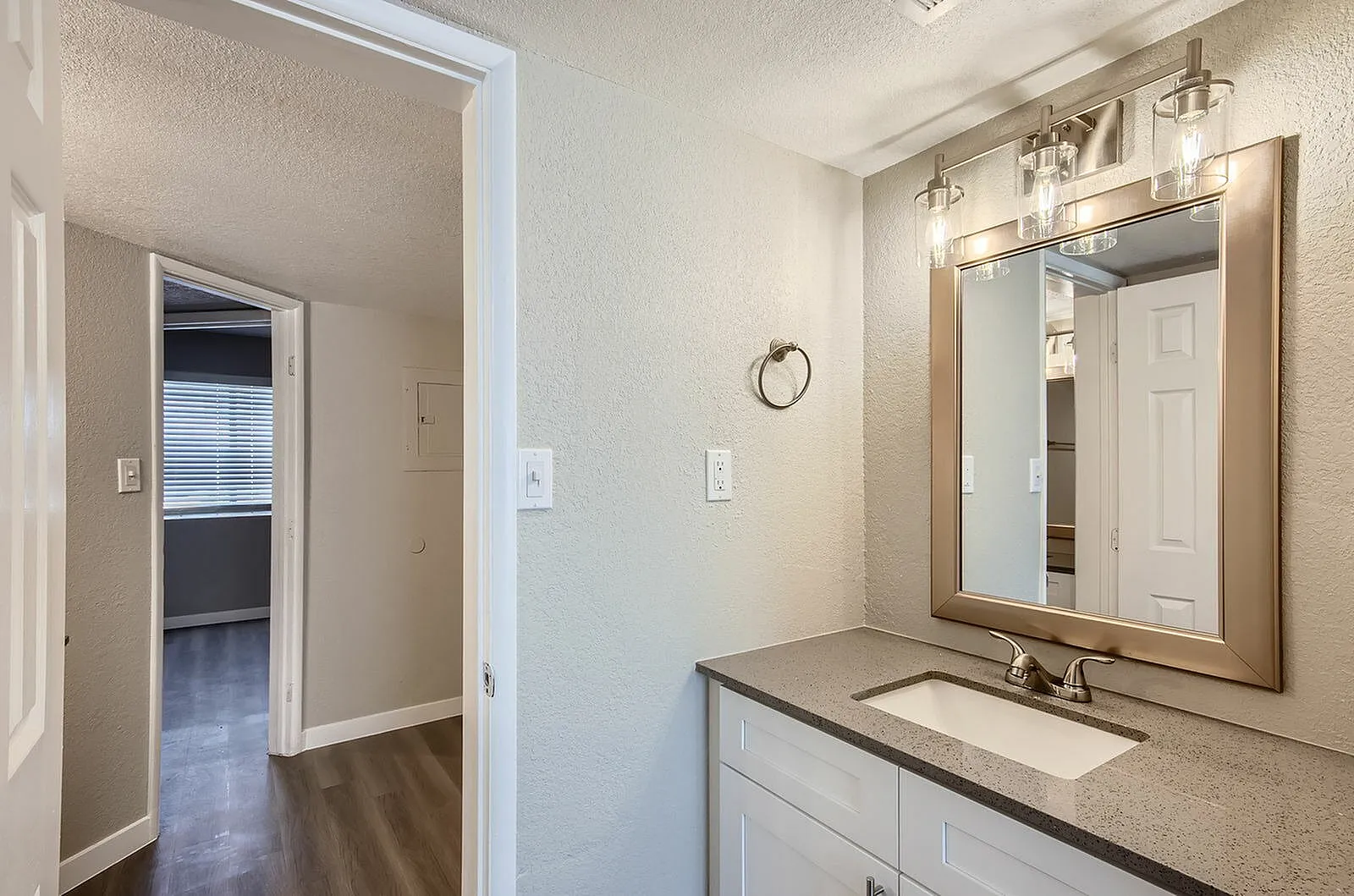 Primary bathroom, white cabinetry, quartz countertops, framed mirror, wall sconces, wood-style plank flooring