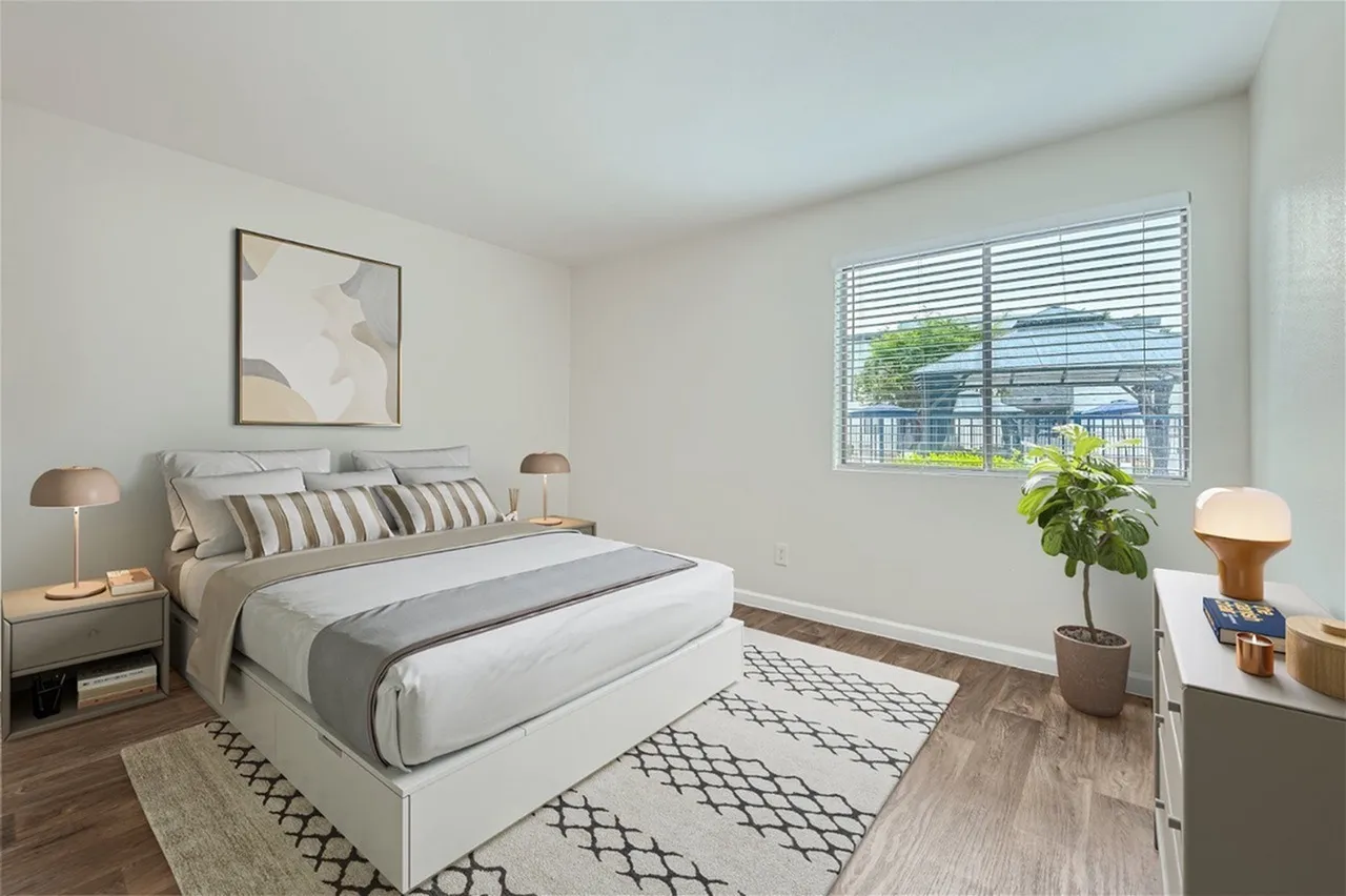 Primary bedroom, wood-style plank flooring, striped bedding, geometric patterned area rug