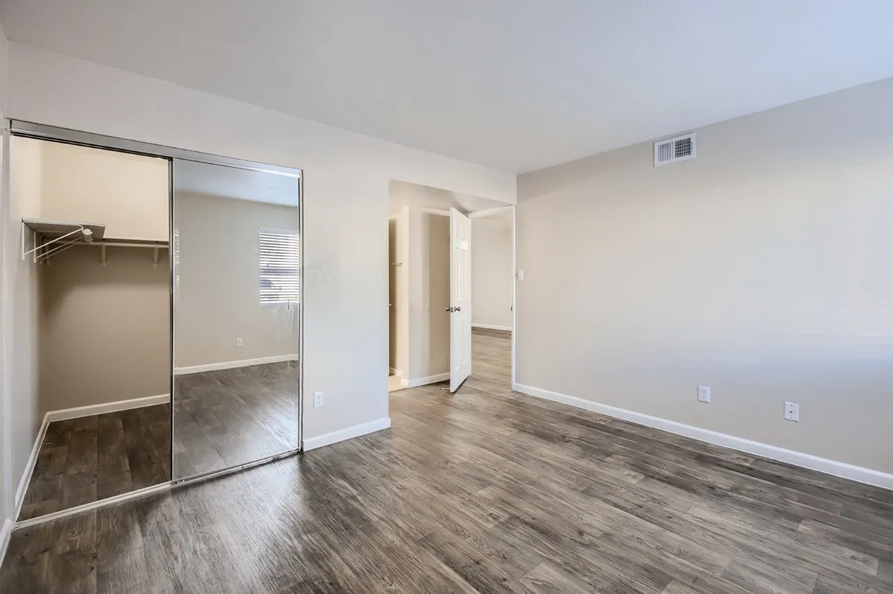Primary bedroom, mirrored sliding closet doors, wood-style plank flooring, white walls
