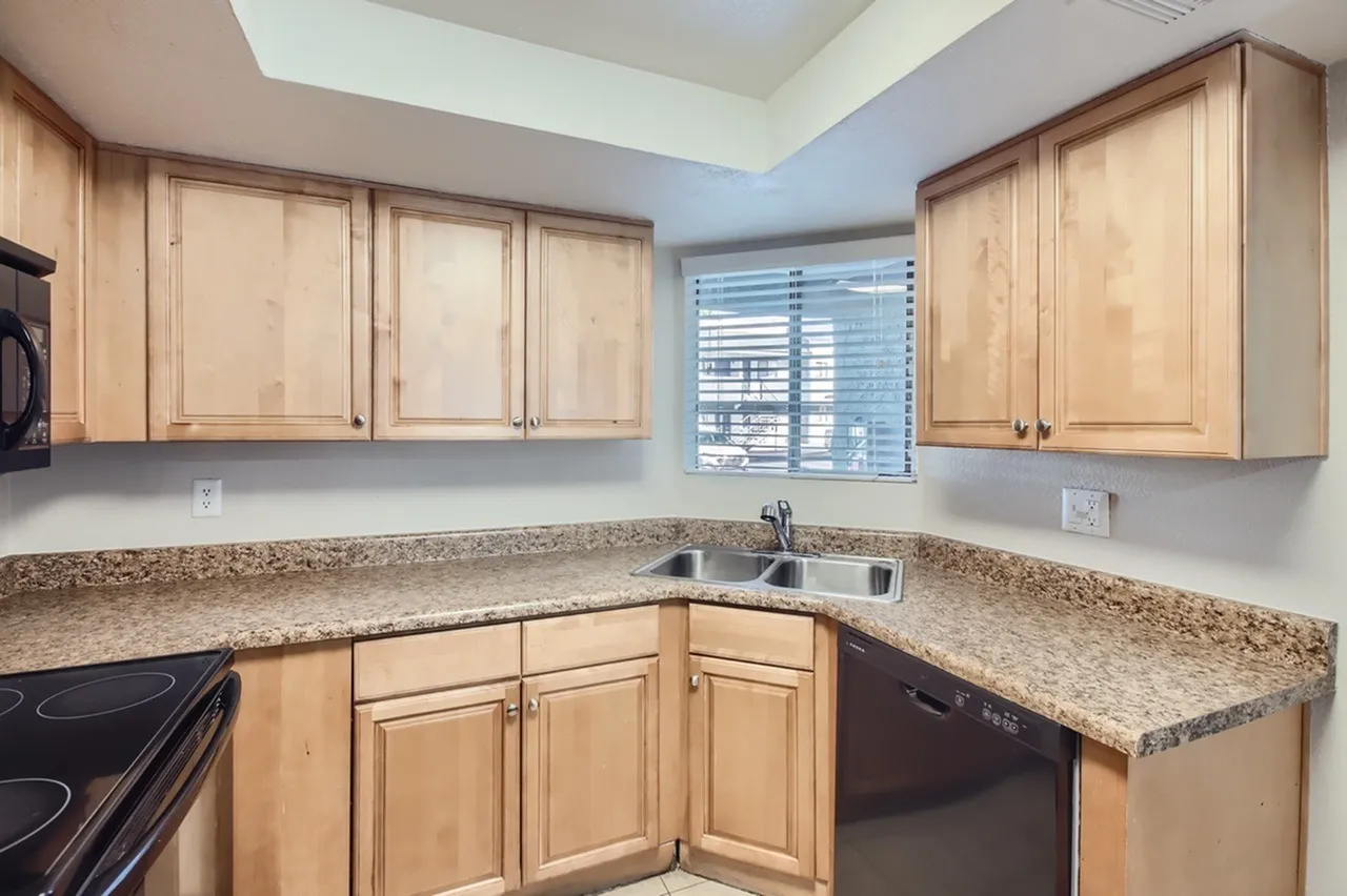 Kitchen, light wood cabinetry, speckled granite countertops, black appliances, window