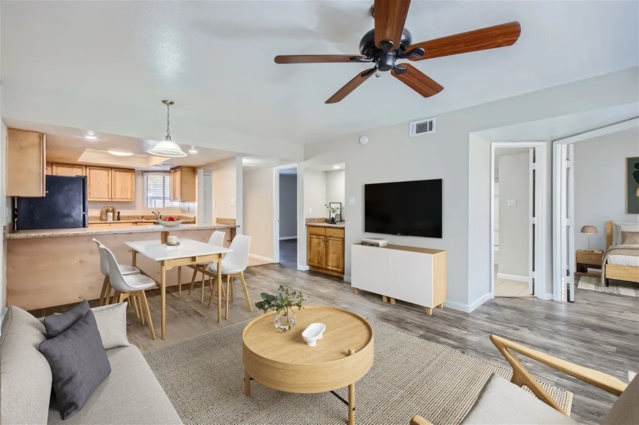 Open-concept living and dining area, wood-style plank flooring, ceiling fan, flat-screen TV, round wood table, kitchen with light cabinetry