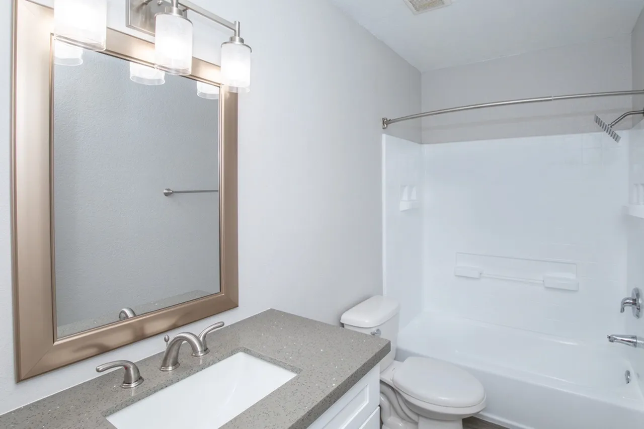 Primary bathroom, gray countertops, framed mirror, white cabinetry, tile shower