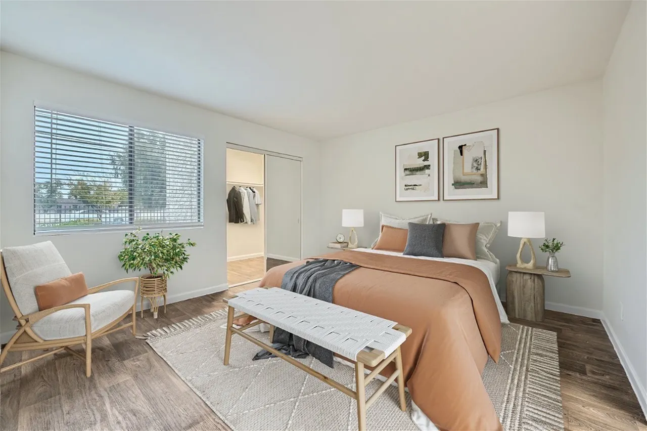 Primary bedroom, wood-style plank flooring, upholstered accent chair, balcony with blinds
