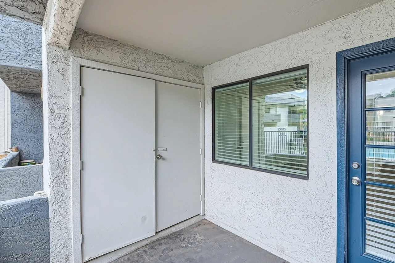 Covered patio with white textured walls, sliding glass doors, windows with horizontal blinds, blue entry door