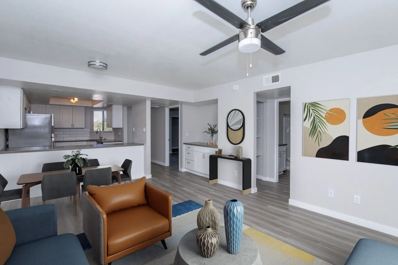 Open concept living area, wood-style plank flooring, tan leather chair, ceiling fan, kitchen with gray cabinetry