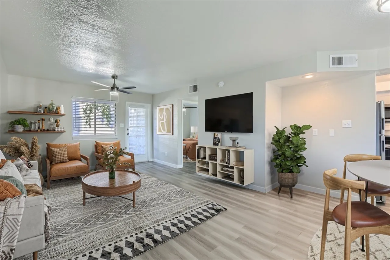 Living room with wood-style plank flooring, ceiling fan, TV wall, tan armchairs, round wood table
