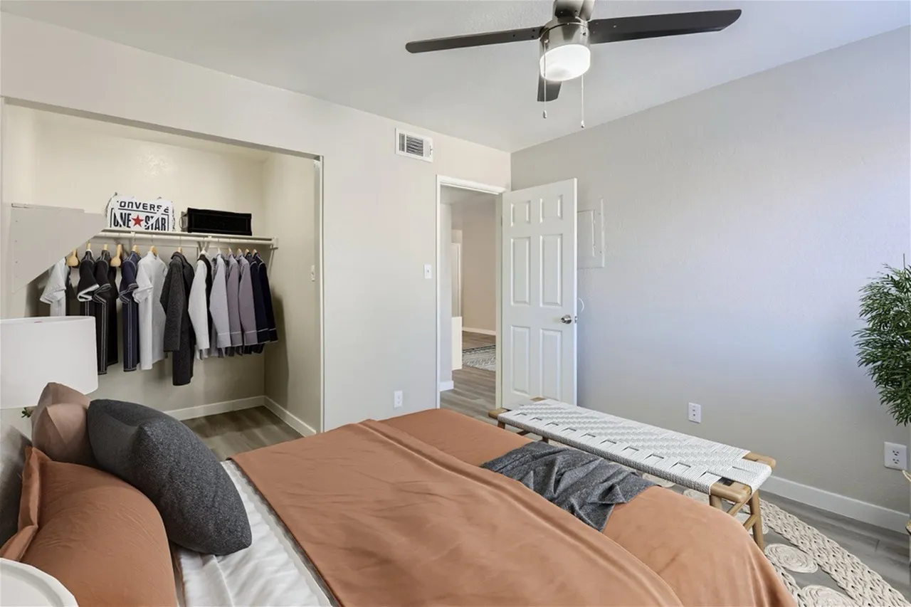 Primary bedroom, wood-style plank flooring, ceiling fan, clothing closet with rod
