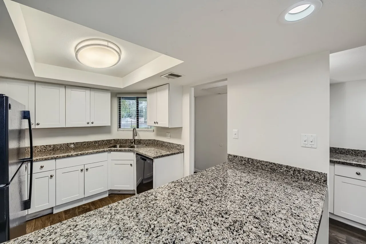 Kitchen, white shaker cabinetry, speckled granite countertops, stainless appliances, wood-style plank flooring