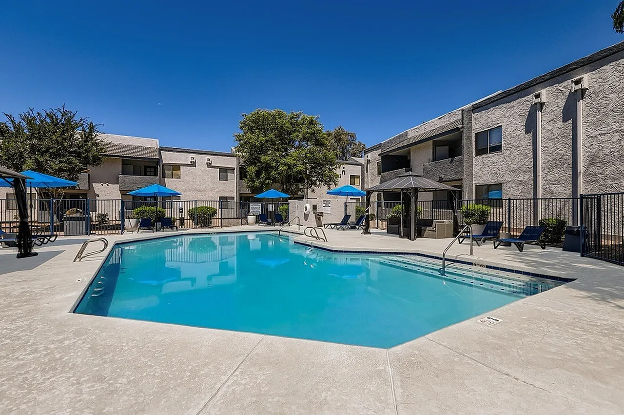 Resort-style pool, blue umbrellas, lounge seating, stone patio, multi-story apartment buildings
