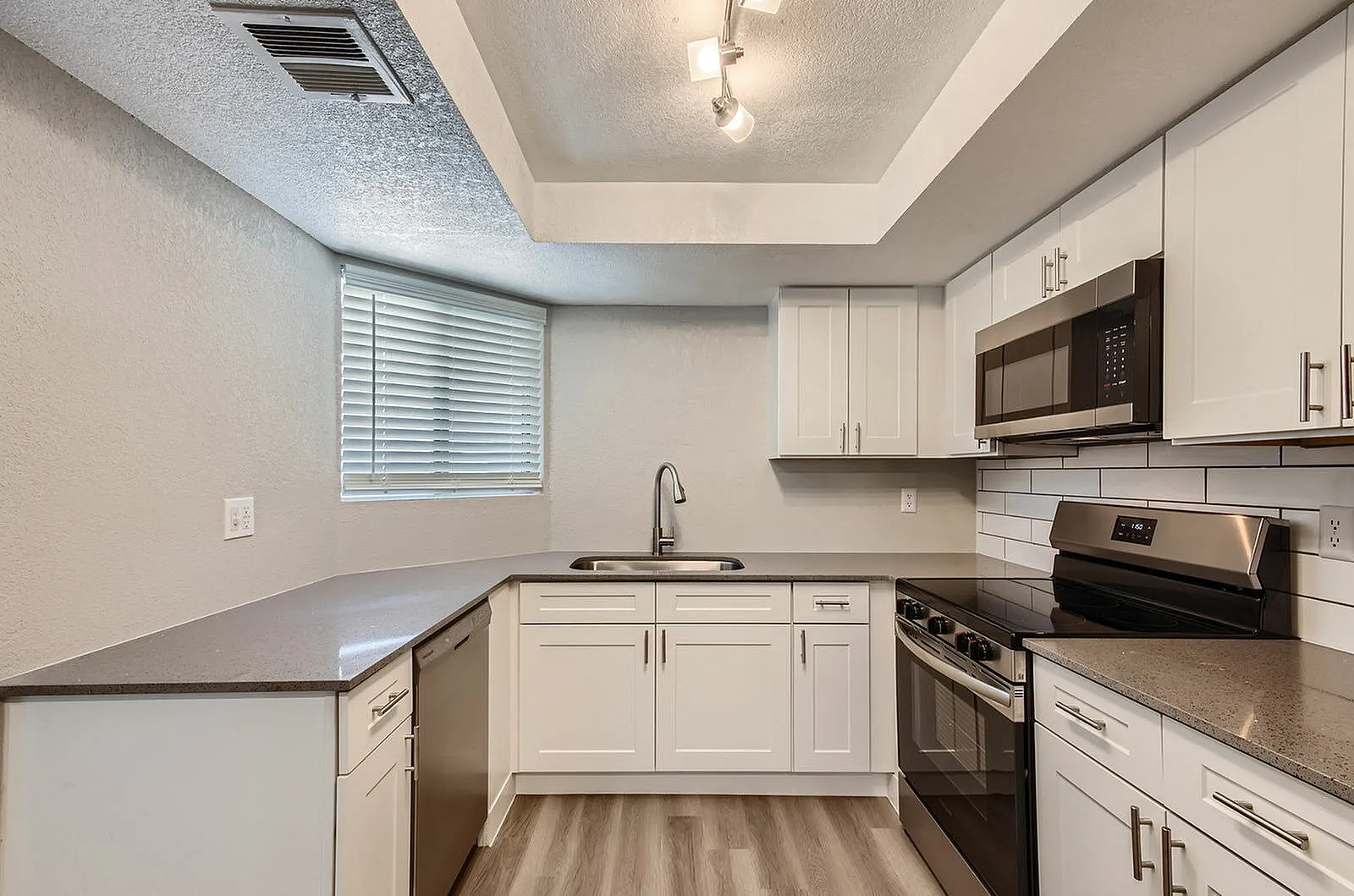 Kitchen, white shaker cabinetry, dark quartz countertops, stainless appliances, wood-style plank flooring