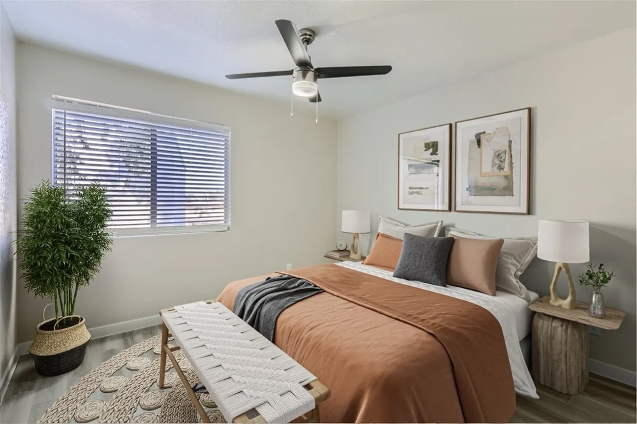 Primary bedroom, wood-style plank flooring, ceiling fan, framed wall art, bedside tables
