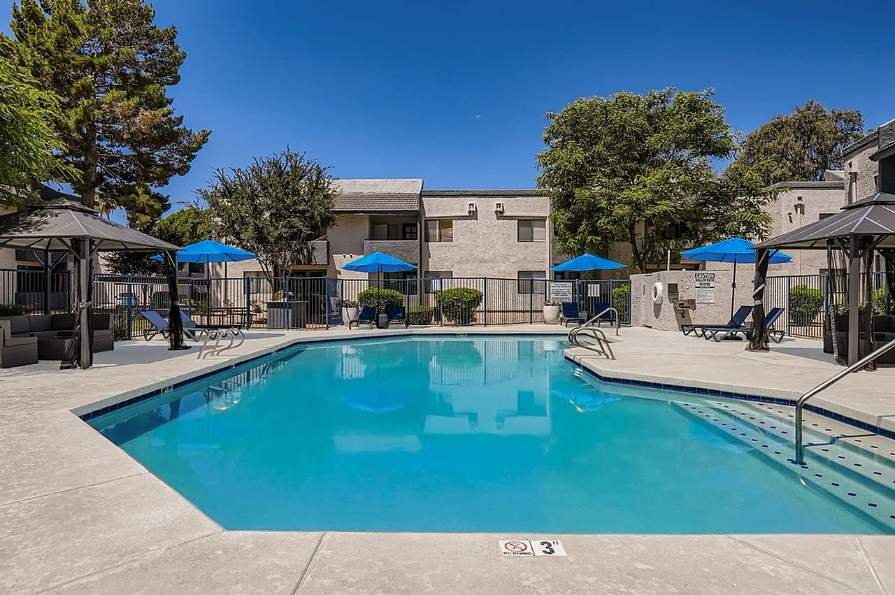 Swimming pool with turquoise water, blue umbrellas, lounge chairs, fencing