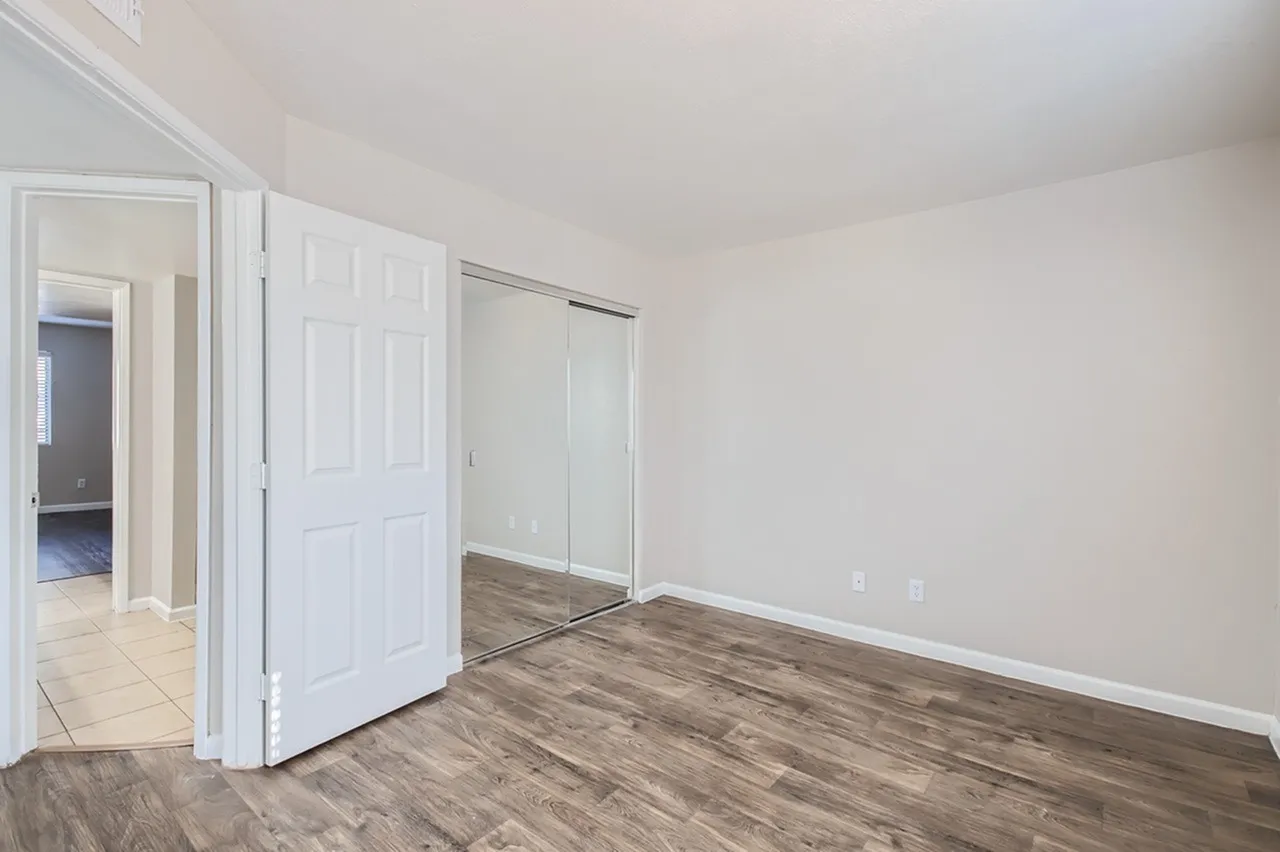 Bedroom, wood-style plank flooring, mirrored sliding closet doors, white six-panel closet