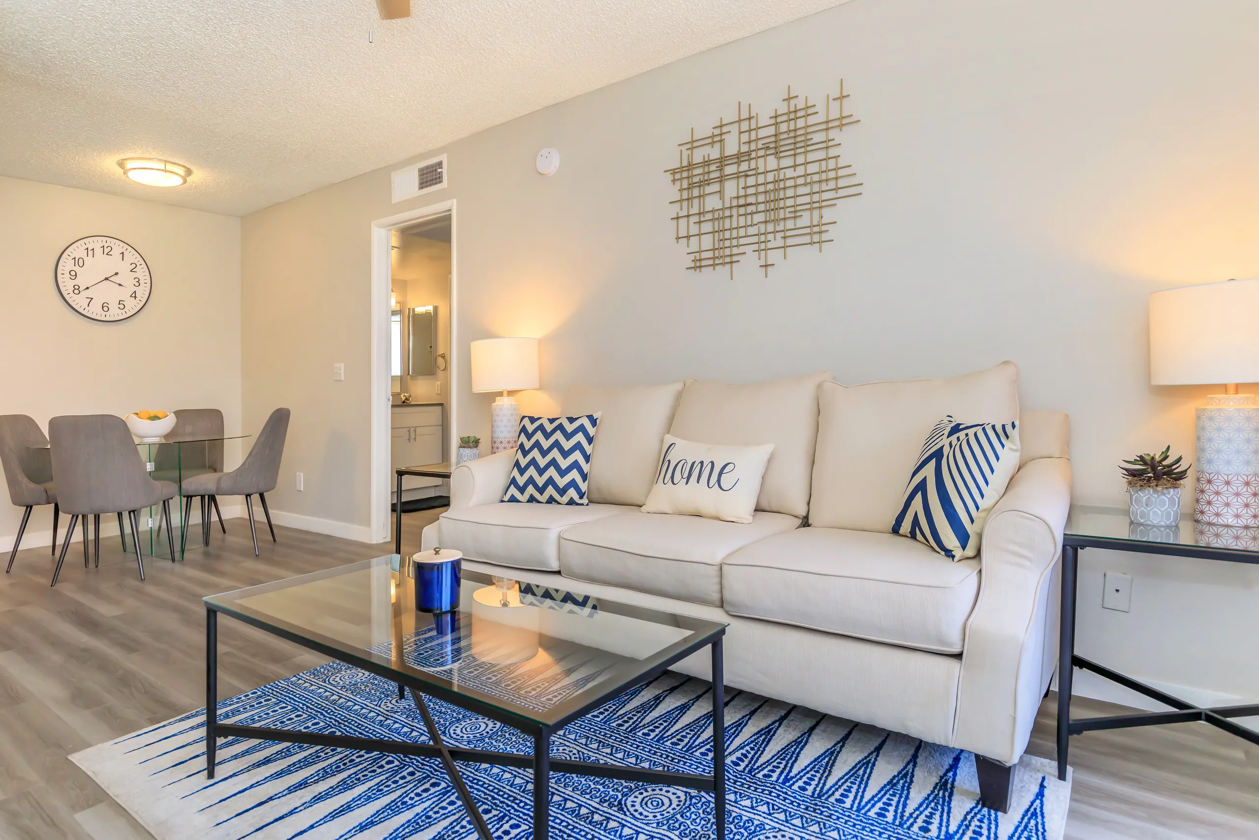 Living room opening into dining area with glass table and wall clock
