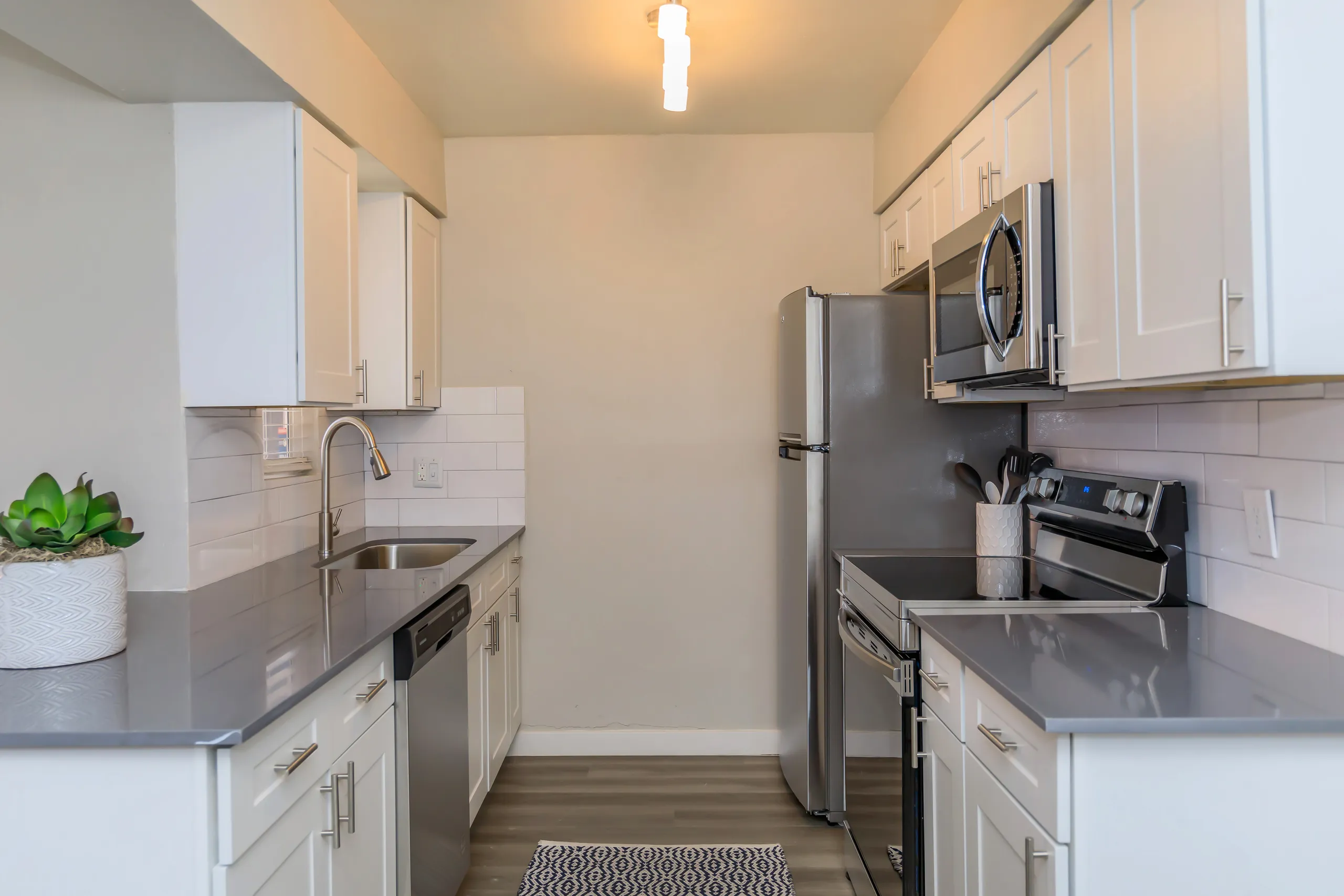 Galley kitchen with white cabinetry, stainless appliances, and subway tile backsplash