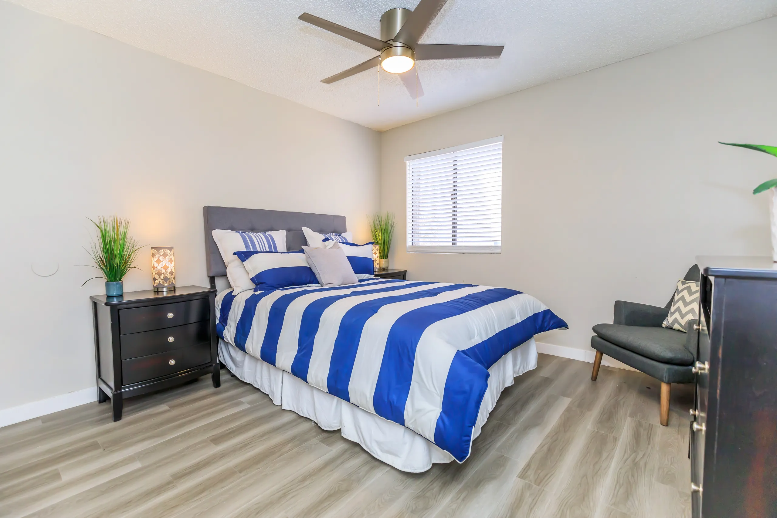 Bedroom with upholstered headboard, ceiling fan, and wood-style flooring