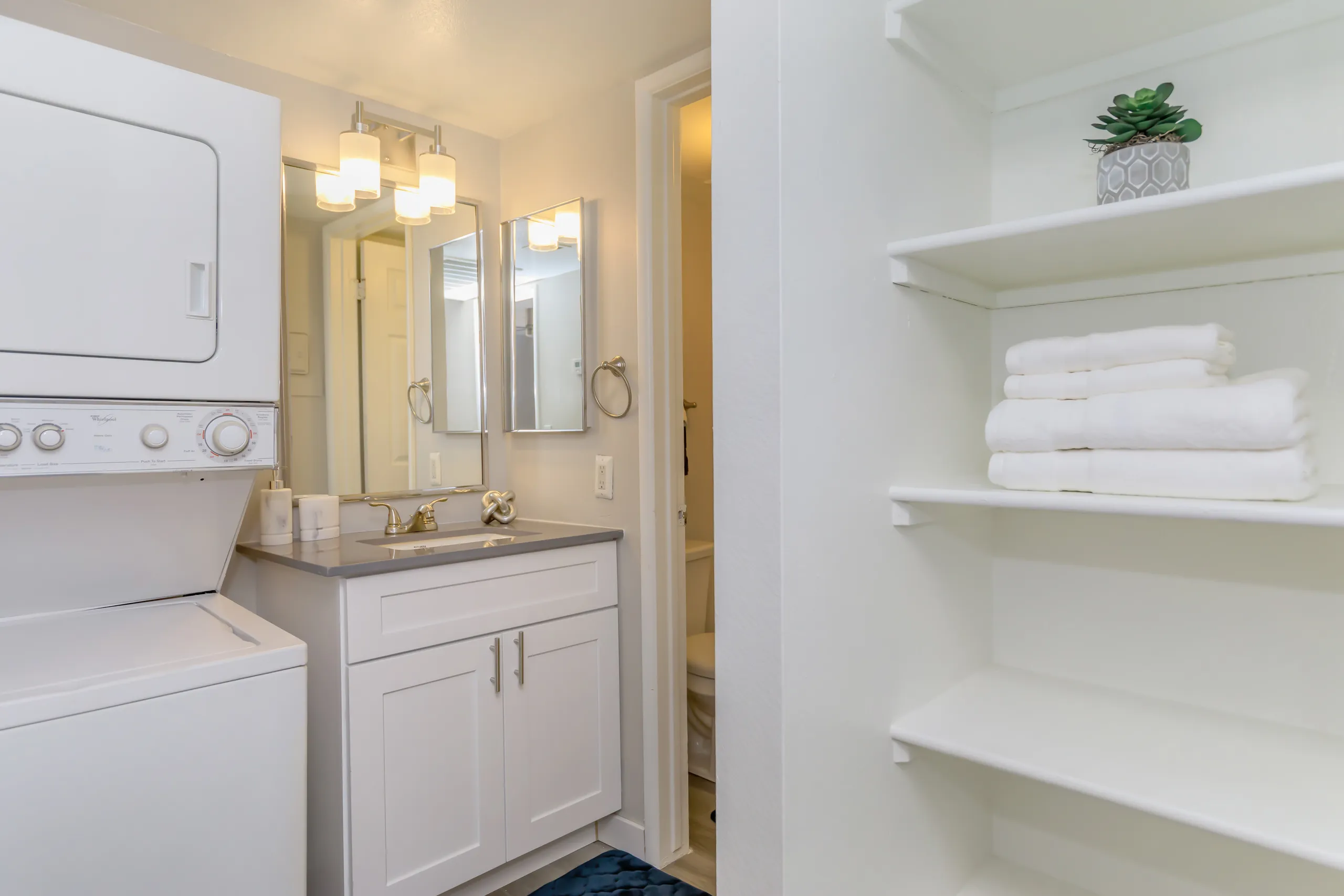 In-unit stacked washer and dryer beside a vanity sink and linen shelving