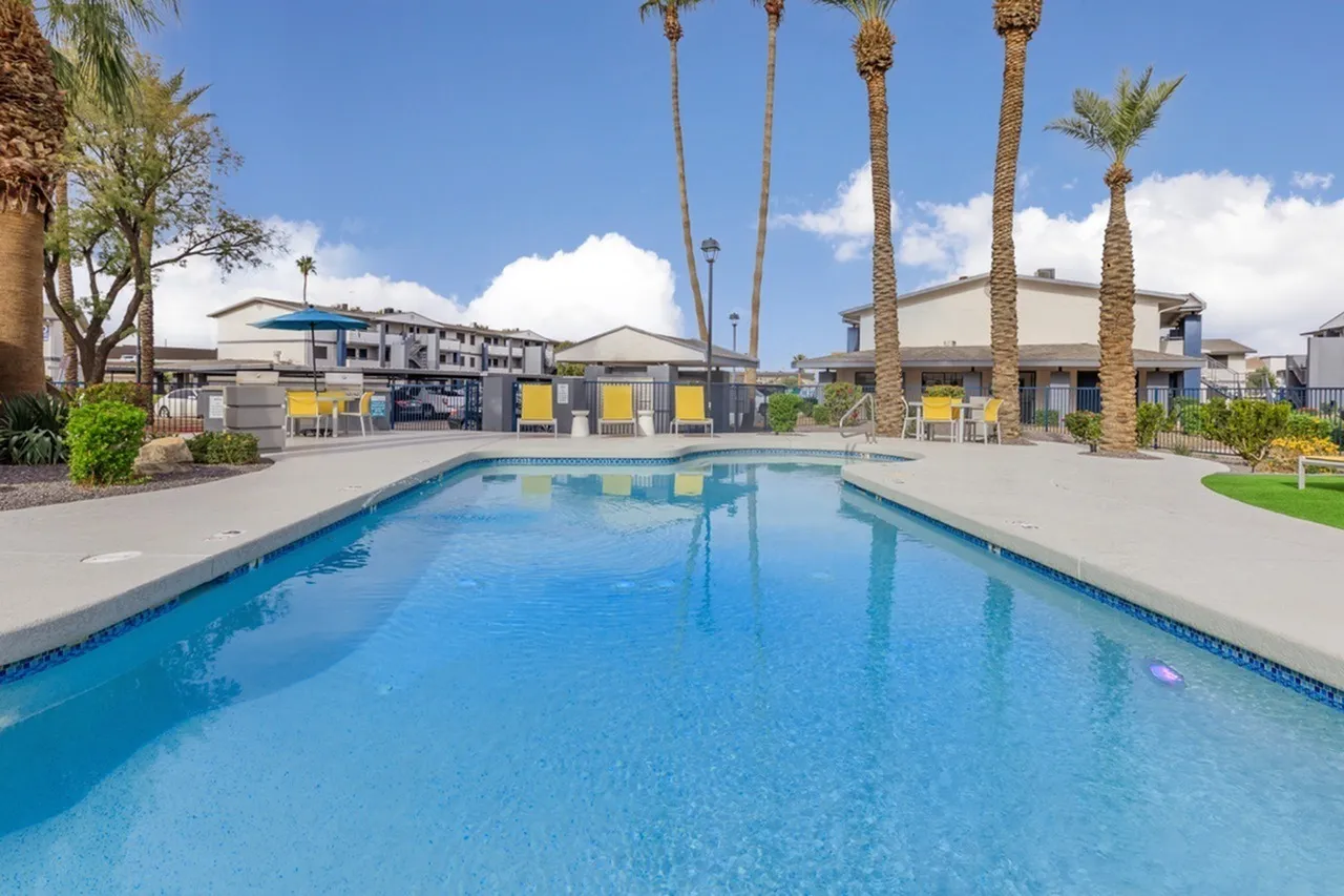Resort-style pool with crystal clear water, lounge chairs, tall palm trees, community buildings