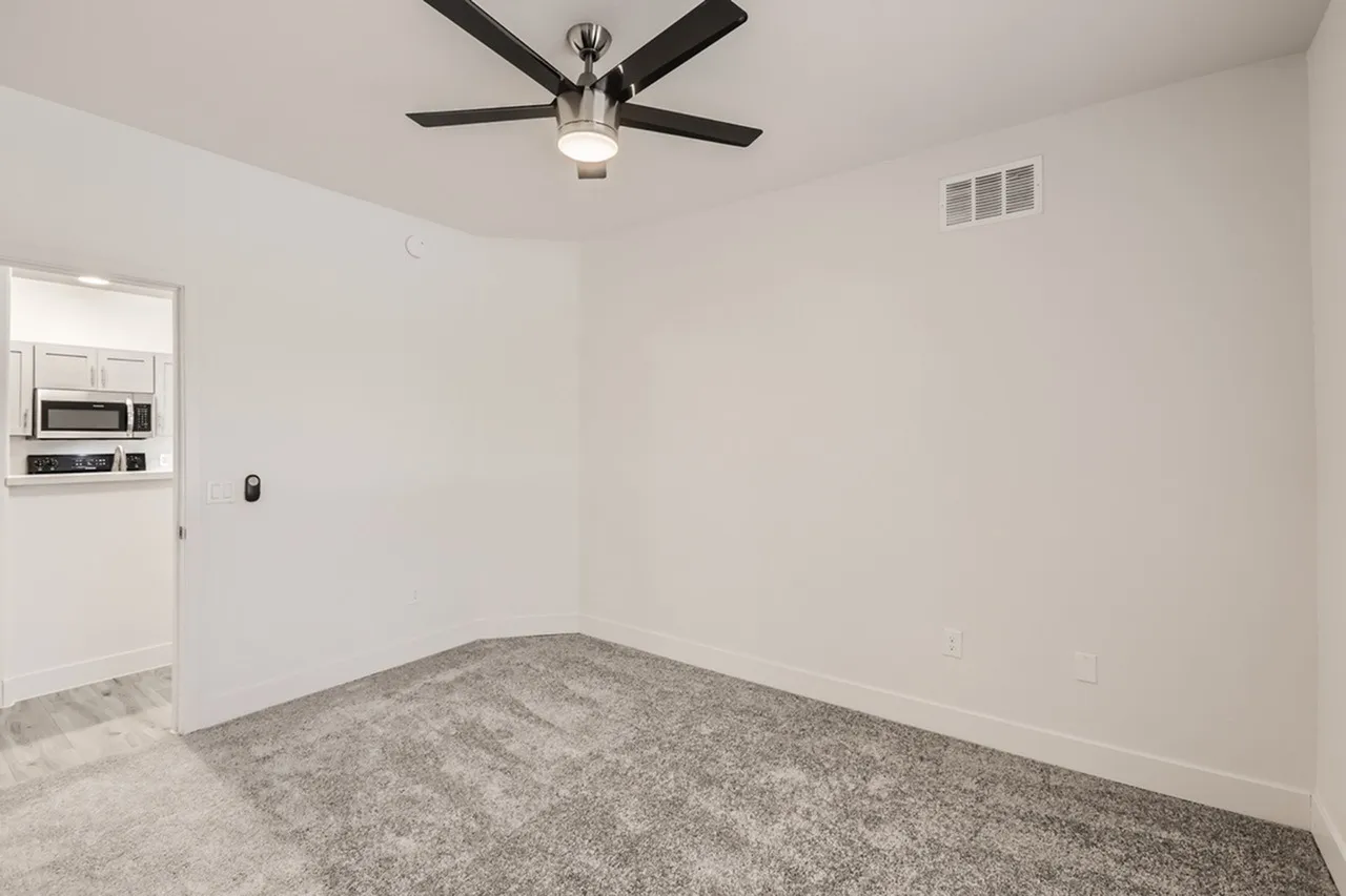 Empty room, gray carpeting, ceiling fan with light fixture, white walls, HVAC vent