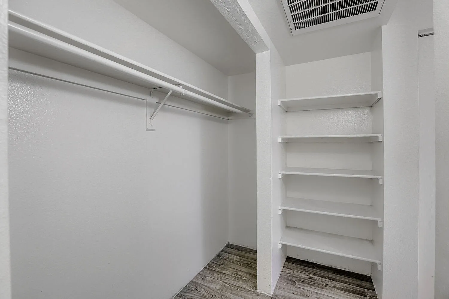 Walk-in closet, metal hanging rod, shelving units, wood-style plank flooring