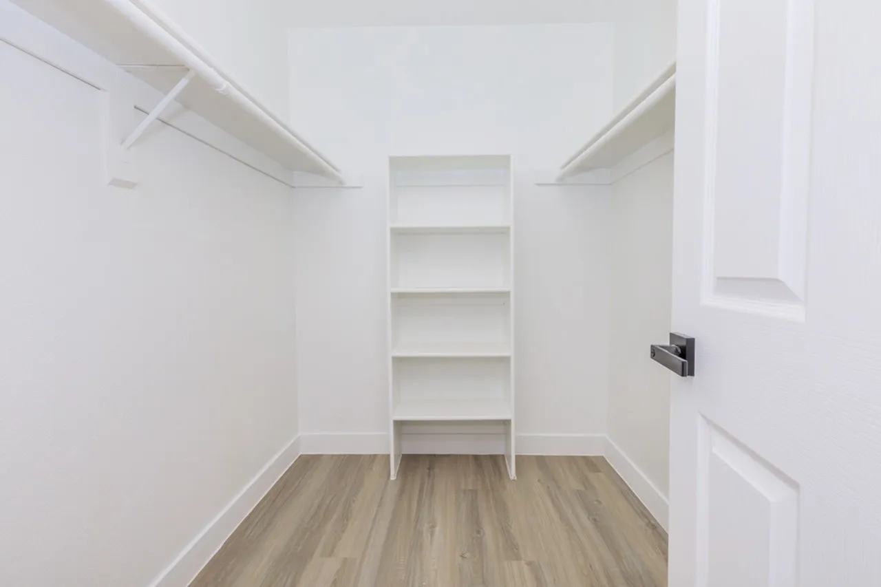 Walk-in closet, white shelving, hanging rods, wood-style plank flooring