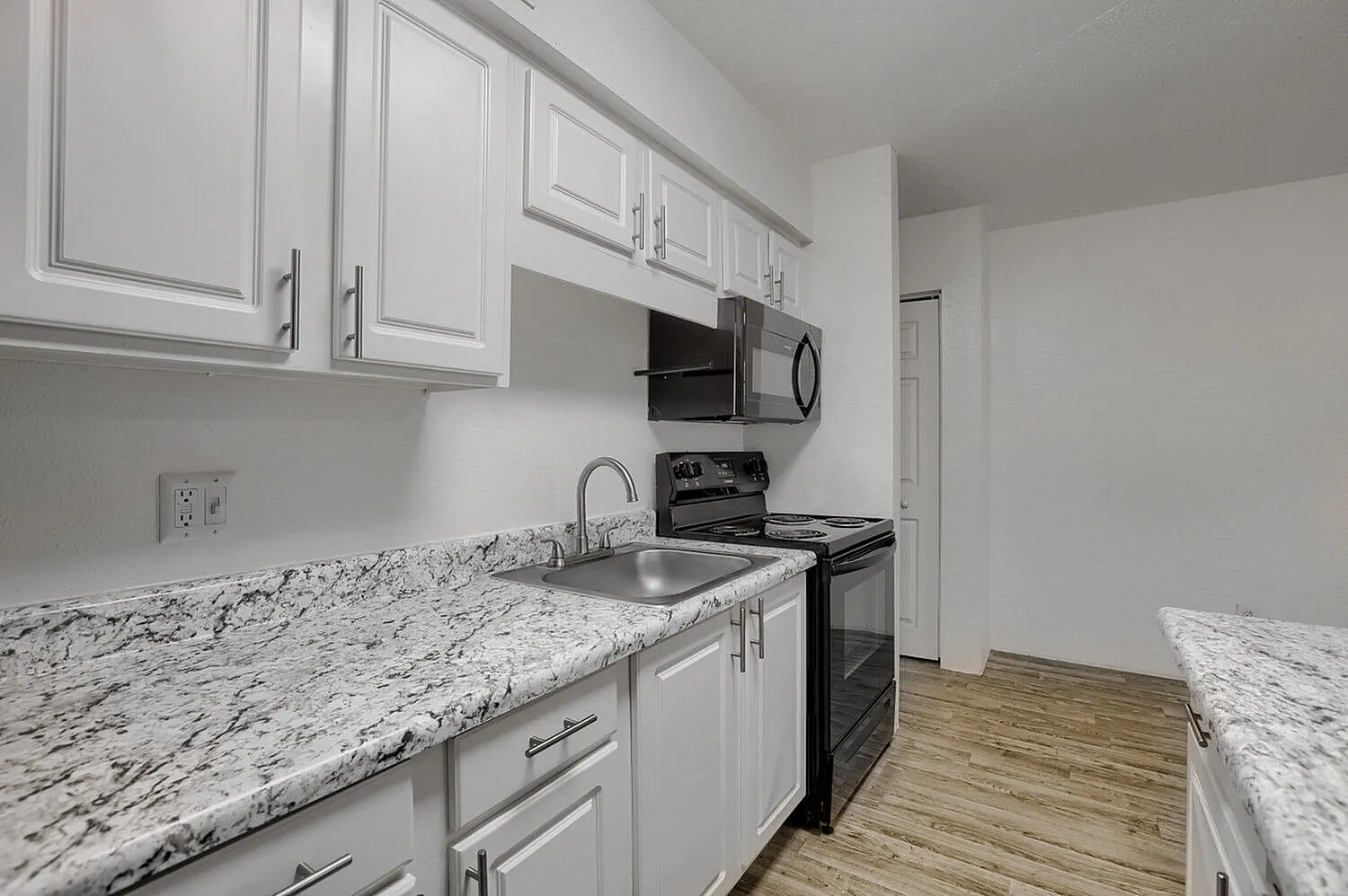 Kitchen, white shaker cabinetry, speckled granite countertops, black range, wood-style plank flooring