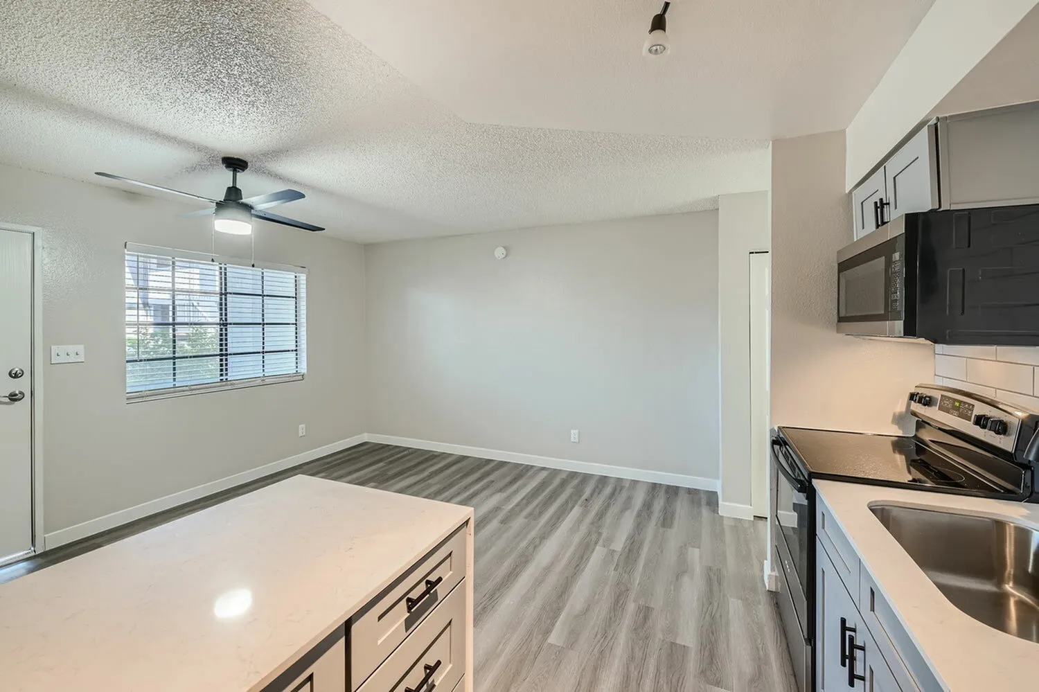 Kitchen with white shaker cabinetry, quartz countertops, stainless appliances, gray wood-style plank flooring