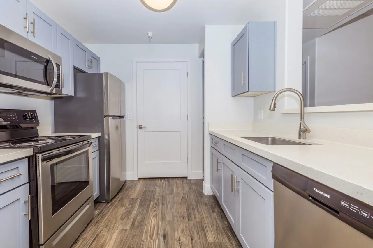 Kitchen, light blue cabinetry, white quartz countertops, stainless steel appliances, wood-style plank flooring