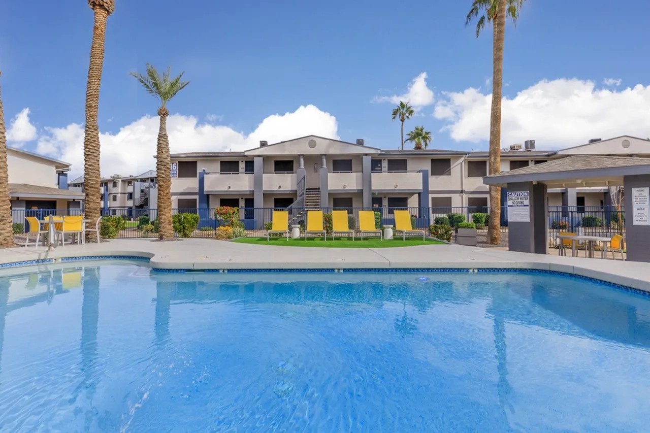 Resort-style swimming pool, lounge chairs, palm trees, multi-story apartment building