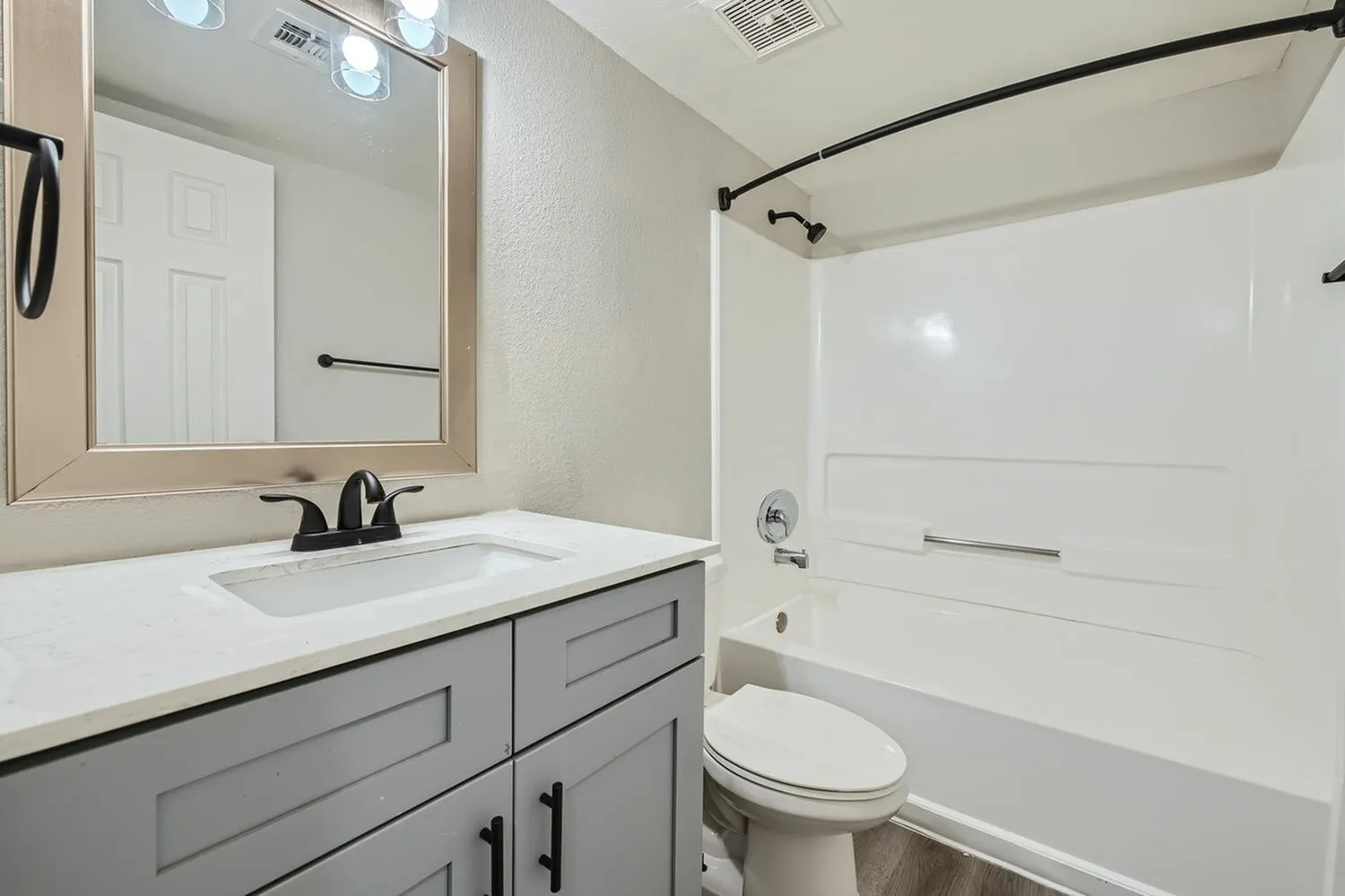 Bathroom with gray vanity cabinetry, white quartz countertop, framed mirror, white subway tile surround, toilet