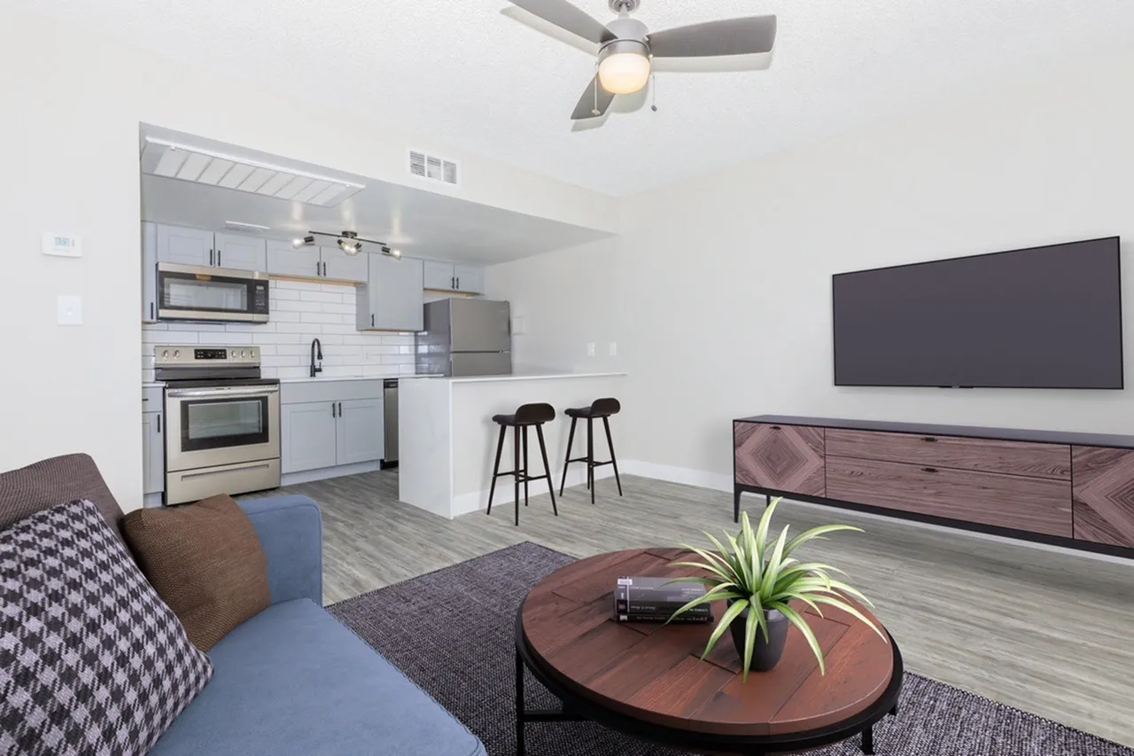 Open concept living and kitchen area, wood-style plank flooring, white shaker cabinetry, stainless appliances, ceiling fan