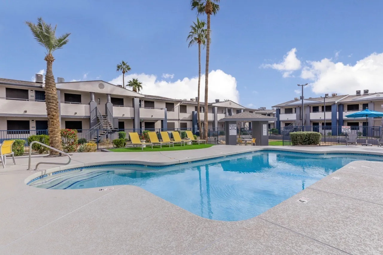 Swimming pool with lounge chairs, palm trees, apartment buildings, clear sky