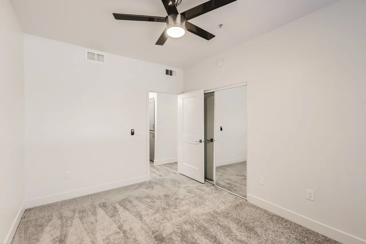 Primary bedroom, gray carpet flooring, ceiling fan, glass doors to bathroom