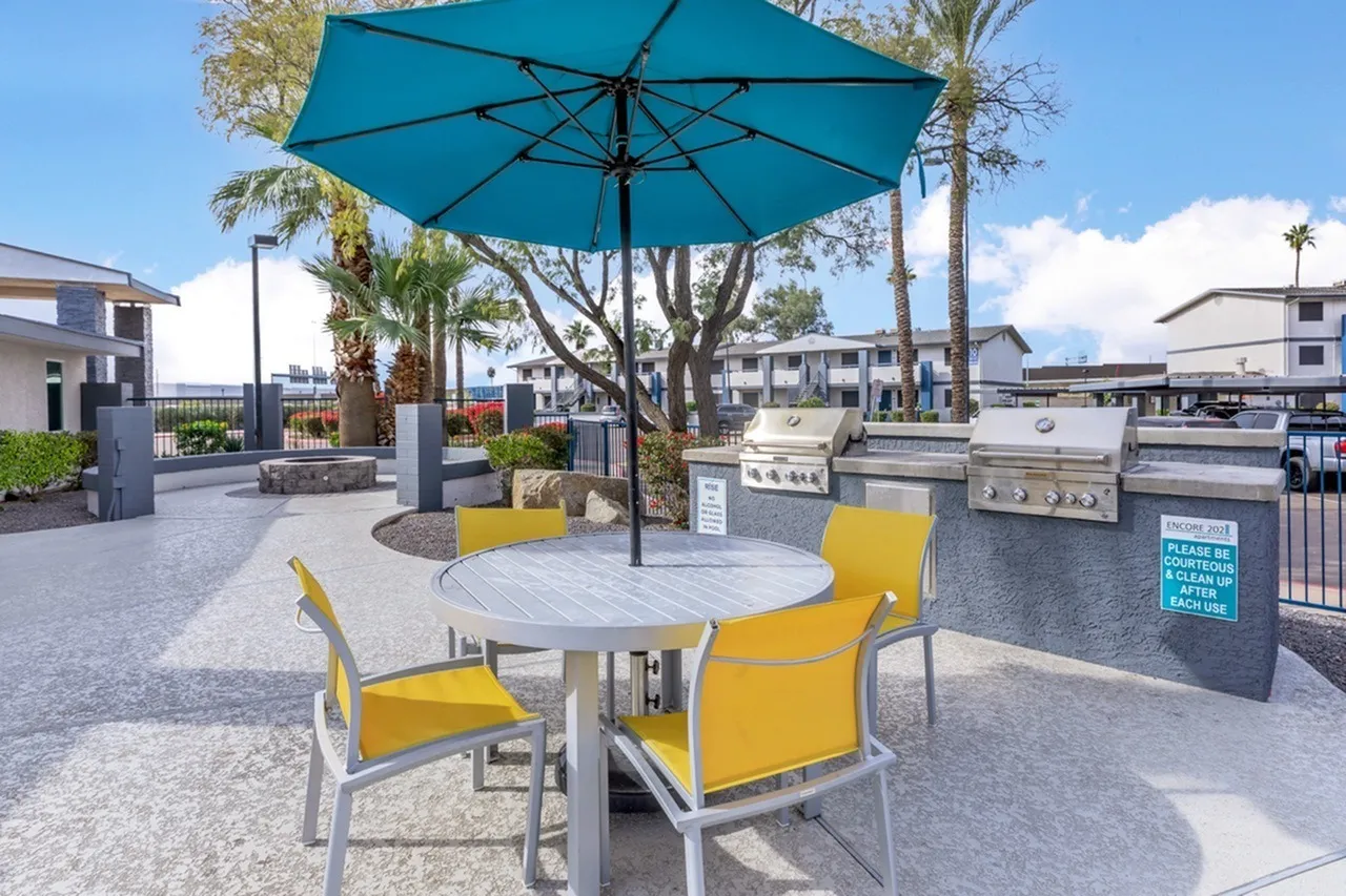 Outdoor patio area, turquoise umbrella, yellow chairs, grills, palm trees