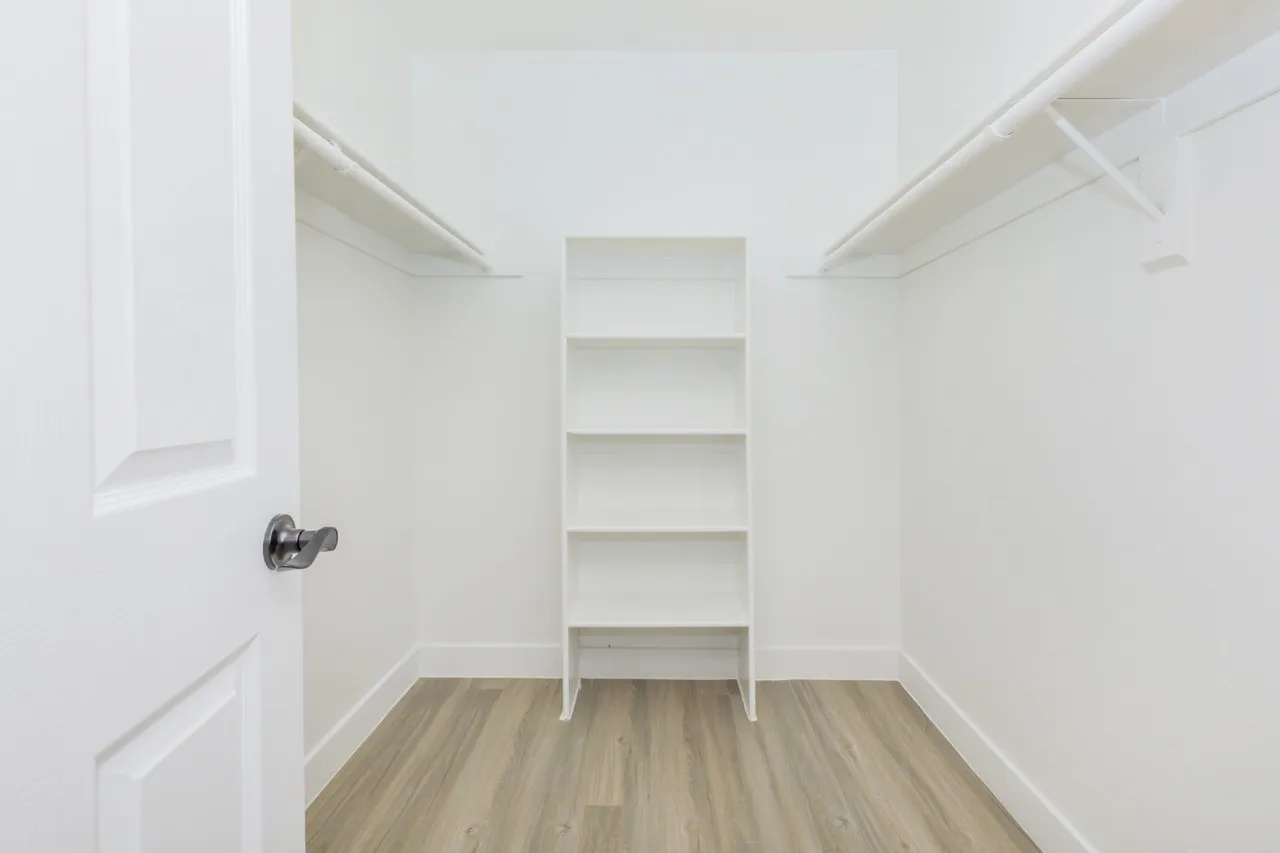 Walk-in closet, white shelving, hanging rods, wood-style plank flooring